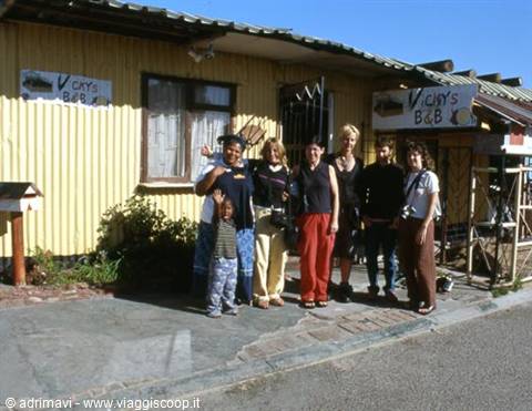 Tourist group in front of Vick's B&B, yellow corrugated metal house, sunny light