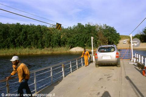 River ferry carrying an SUV with workers in orange overalls between green banks