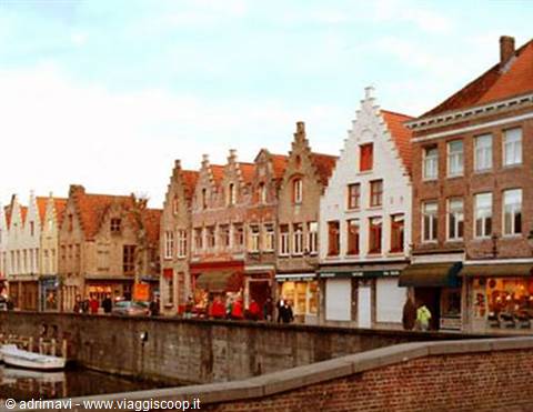 Stepped brick facades along Bruges canal, moored boats under blue sky