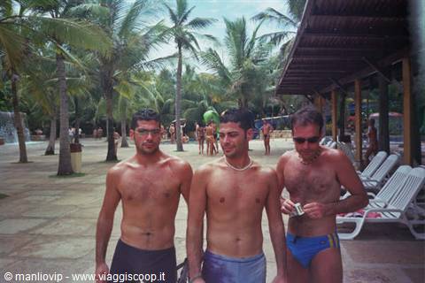 Three young men by the pool among palm trees and sun loungers