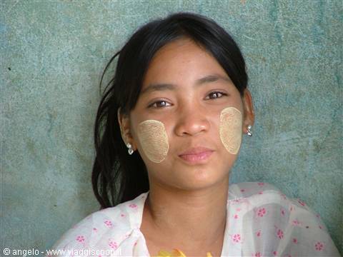 Girl with thanaka circles on cheeks in front of green wall