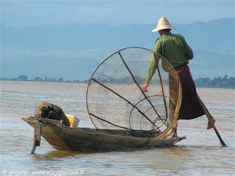 Fisherman with conical net basket balancing on wooden boat, Inle Lake