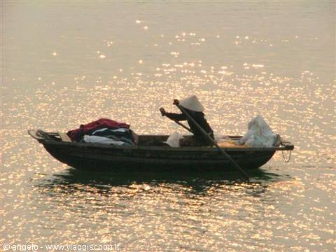 Wooden boat with conical-hat fisherman rowing on shimmering golden water
