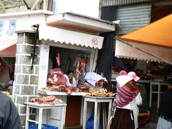 Woman in colorful shawl buying meat at an outdoor butcher stall