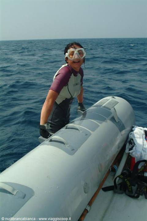 Woman in wetsuit and mask climbs back onto gray inflatable boat from open sea