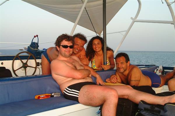 Four friends in swimwear relaxing on a catamaran's blue cushions at sea