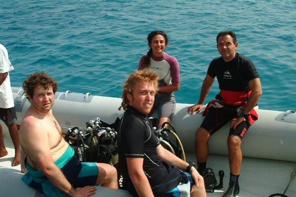 Four divers in wetsuits on inflatable boat, scuba gear, turquoise sea