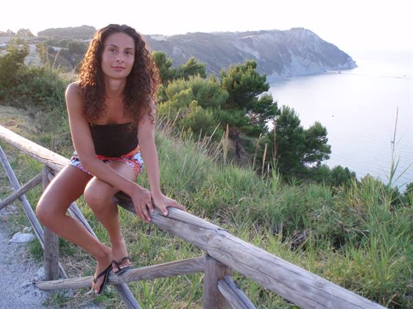 Curly-haired woman sitting on a wooden fence above the bay