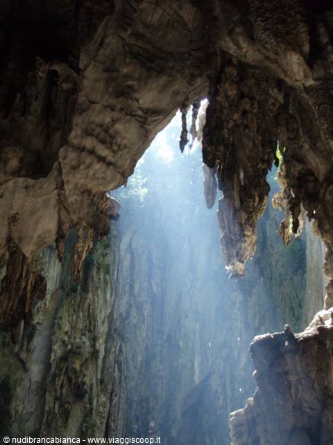 Sunbeams pour through the cave mouth among limestone stalactites, Batu Caves