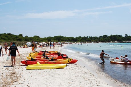 Colorful kayaks on white sand, bathers and a boy playing with a ball