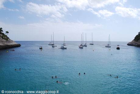 Swimmers and anchored sailboats in a turquoise cove between white cliffs