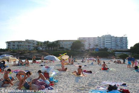 Beachgoers on white sand with umbrellas, hotels and pines behind