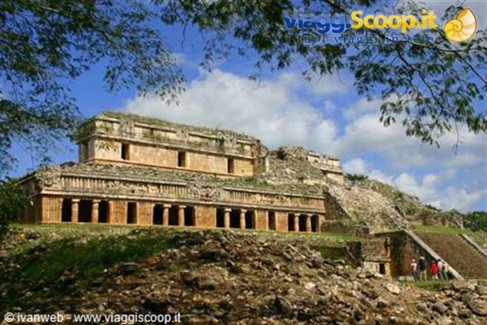 Stone Maya temple at Sayil, carved columns on green hill under white clouds