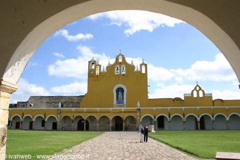 Yellow convent of Izamal framed by an arch, people walking on the path