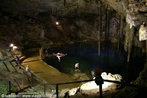 Swimmers and visitors inside a cenote cave with stalactites and artificial lights