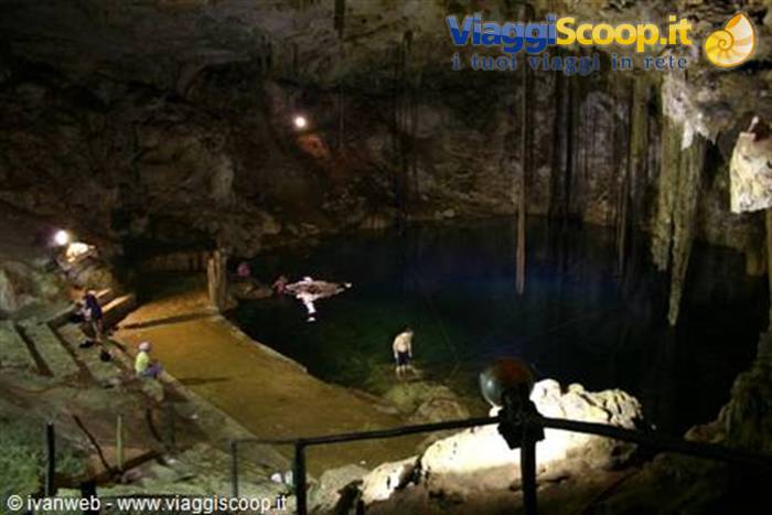 Swimmers and visitors inside a cenote cave with stalactites and artificial lights