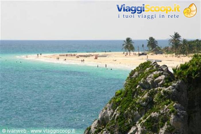 White sand beach with palm trees, swimmers in turquoise water, green rocks below