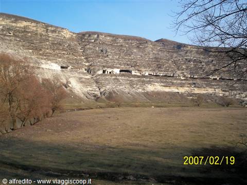 Caves carved into limestone cliffs above the grassy field at Orheiul Vechi