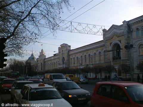 Traffic in front of a yellow historic building with Christmas decorations overhead