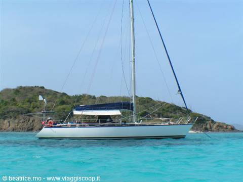 White sailboat anchored in turquoise water by a green islet