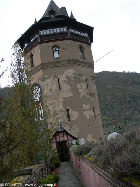 Medieval plastered stone tower under grey sky, shrubs along the stone path