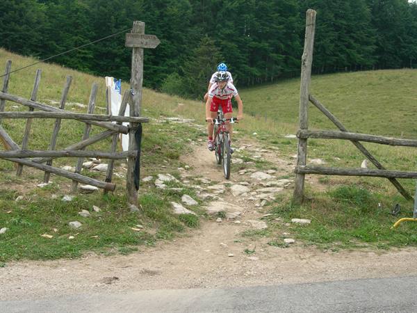 Mountain bikers ride through a wooden gate on a rocky dirt trail