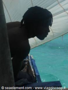 Man on a wooden sailing boat, turquoise sea beneath the sail