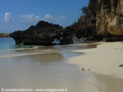 Rocky cliff over white sand beach, turquoise sea under blue sky