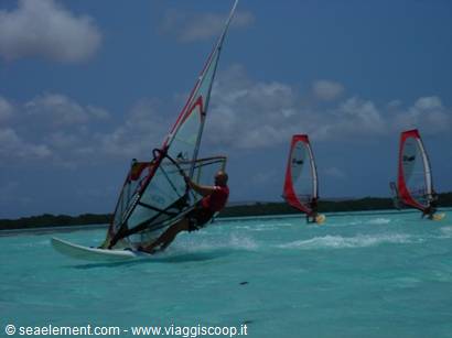 Windsurfers on turquoise lagoon, red sails under cloudy sky