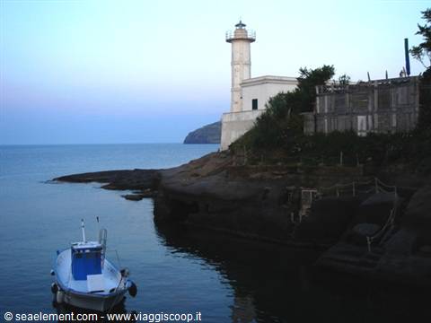Old white lighthouse on the rocks, blue boat moored in the cove