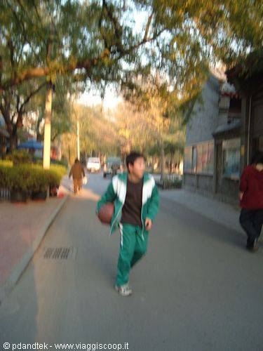 Boy in green tracksuit runs with basketball along a tree-lined street