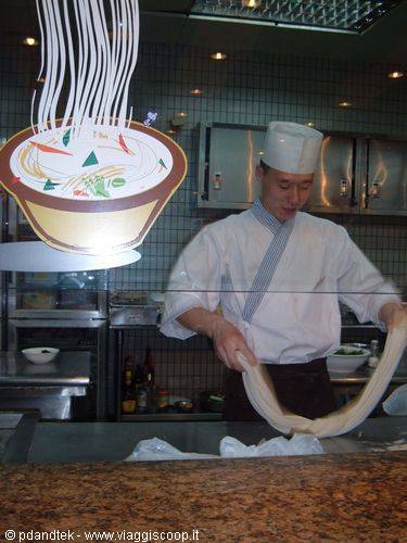 Chef in white pulling fresh noodles behind the kitchen glass