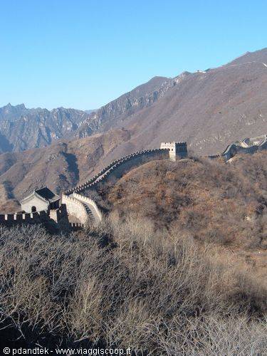 The stone Great Wall snakes across brown mountains under a blue sky