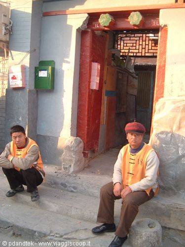Two men in yellow vests rest outside a traditional red doorway