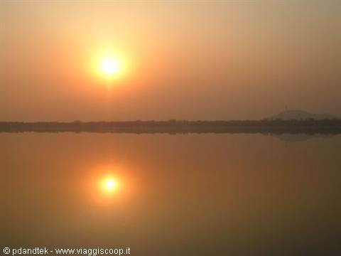 Low sun reflected on calm lake, dark shore and orange sky
