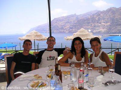 Four friends sitting at a set table by the sea under straw umbrellas