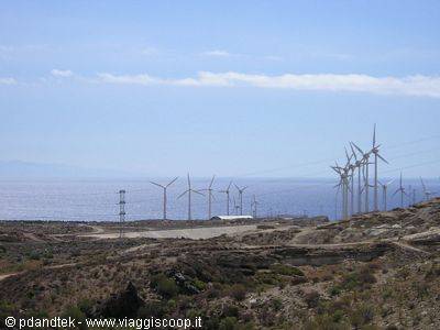 Wind turbines on arid hills by the sea under blue sky