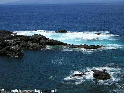 Black lava rocks beaten by foamy waves of the deep blue ocean