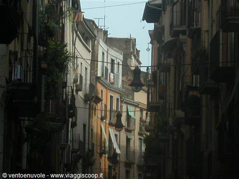 Narrow alley between old balconied buildings, hanging streetlamps, soft light