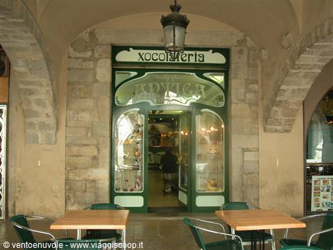 Art Nouveau green entrance of Amatller chocolate shop under stone arches, outdoor tables