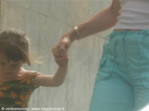 Little girl in floral dress holding a woman's hand, turquoise trousers