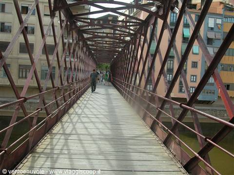 Tourist walks across Girona's Eiffel bridge, red iron lattice over the river