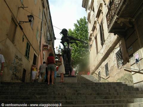 Stone staircase between old buildings, tourists photograph a bronze statue