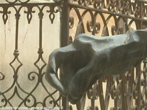 Bronze statue hand pointing in front of a wrought iron gate