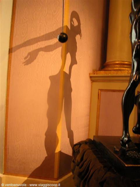 The shadow of a bronze sculpture stretches across the pink wall of a hall