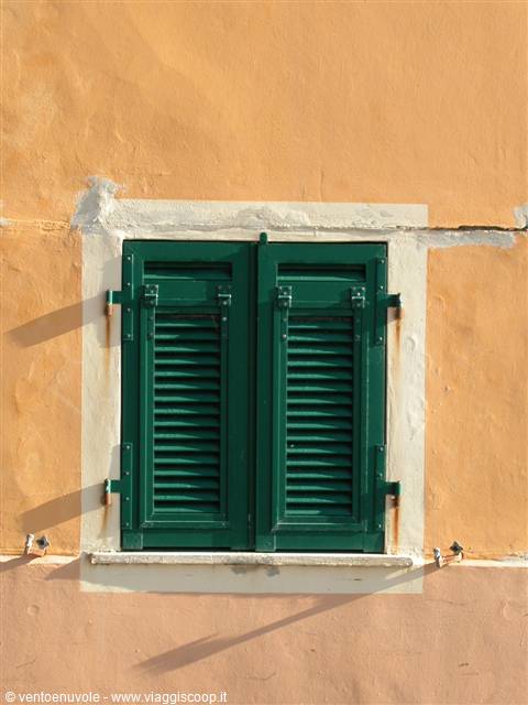 Window with green wooden shutters on ochre plastered facade