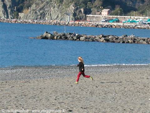 Child running on the sandy beach, sea and rocky cliffs behind