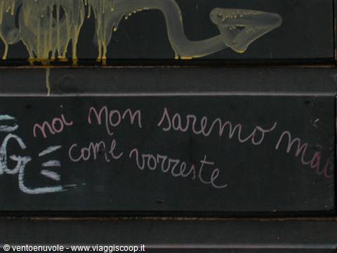 Pink chalk writing on dark shutter: 'we will never be as you want'