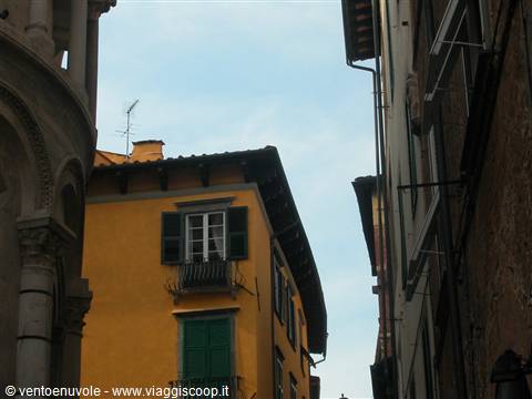 Yellow house with green shutters among old buildings in Lucca