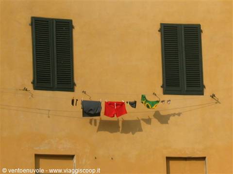 Laundry drying on a line between two green-shuttered windows on ochre wall